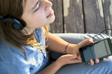 Teen girl with earphones enjoying music from a smartphone outdoors