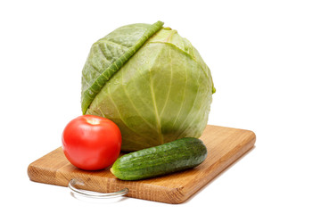 Green cabbage head, tomato and cucumber on wooden cutting board