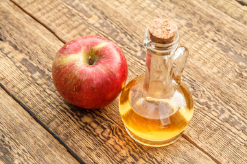 Apple vinegar in glass bottle and fresh red apple on wooden boards