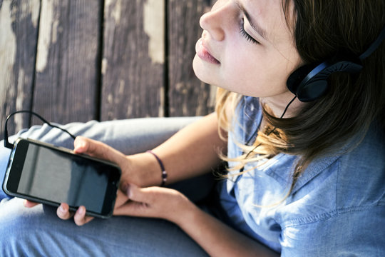 Teen girl with earphones enjoying music from a smartphone outdoors