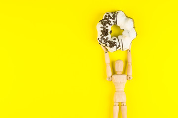 Wooden dummy holding Donut made at home on yellow background.High energy foods to work.Foods with very high calories, sugars.