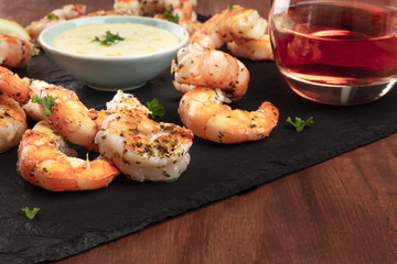 A closeup photo of plate of cooked shrimps with a sauce and a glass of wine, with copy space