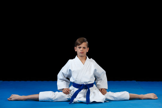 Karate kid wearing white gi and belt in a side split side straddle Chinese split, with arms crossed on