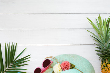 Concept of tropical fruit. Pineapple, straw hat, sunglasses and palm branch on wood plank white color. Summer vacation background and top view design