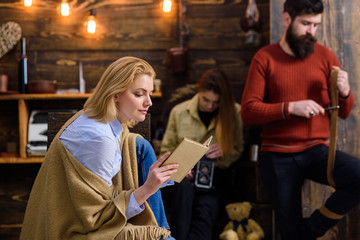Beautiful woman with blond hair reading interesting book. Bookworm absorbed by fantasy world adventures, literature concept. Bearded lumberjack sharpening knife. Teenage girl playing with tin box