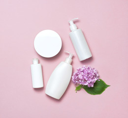 Obraz na płótnie Canvas Cosmetic bottle containers with hydrangea flower on a pink minimalistic background flat lay. Blank label for branding mock-up. Natural beauty product concept.