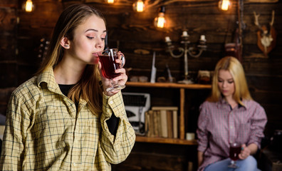 Friends enjoy mulled wine in warm atmosphere, wooden interior. Girls relaxing and drinking mulled wine. Rest and relax concept. Friends on relaxed faces in plaid clothes relaxing, defocused