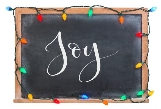 Joy written in white calligraphy lettering chalk on a black chalkboard surrounded with colorful bulb lights isolated on white