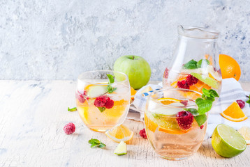 Summer cold cocktail, fruit and berry white sangria with apple, lemon, oranges and raspberry. light concrete background, copy space