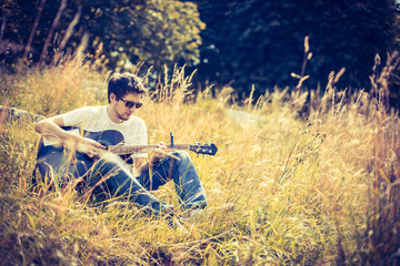 Junger Mann sitzt in der Wiese und spielt Gitarre