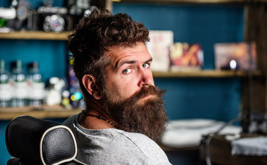 Man with beard and mustache sits in hairdressers chair, beauty supplies on background. Man with...