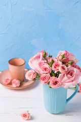 Pink roses flowers in blue cup  and cup for coffee against  blue textured wall.