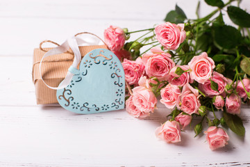 Pink roses flowers, decorative heart and  box with present on white wooden background.