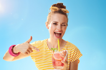 smiling woman against blue sky pointing at refreshing cocktail