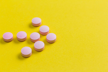 Heap of pink capsules on yellow background.