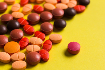 Heap of assorted orange and red capsules on yellow table.