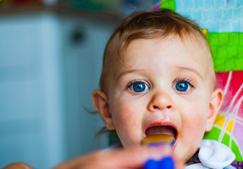 baby boy eating food with spoon at home