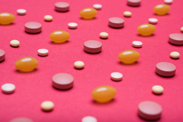 Assortment of various colourful pills on red coloured background. Medication and prescription pills close up background.
