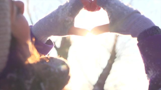 Winter joyful girl showing heart sign and smiling. Beauty teenage model girl having fun in winter park. Slow motion 4K UHD video 3840x2160