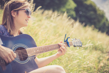 Junges Mädchen sitzt in der Wiese und spielt Gitarre, Singen