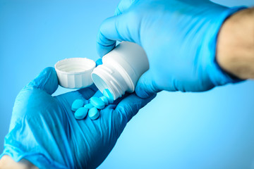 Unknown doctor pours the blue pills out of the bottle into hands