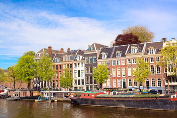 Fototapeta na wymiar Cityscape view of the canal of Amsterdam in summer with a blue sky, house boats and traditional old houses. Picturesque of Amsterdam, North Holland, The Netherlands.