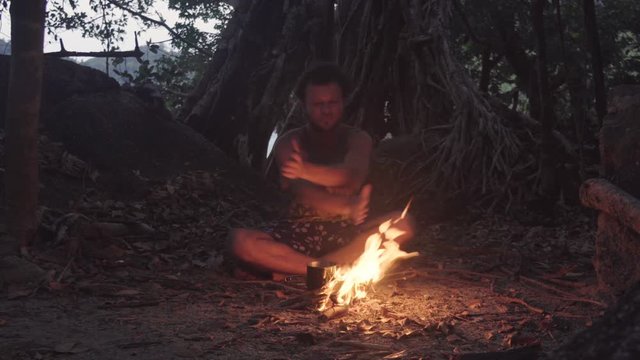 Caucasian Man Burning Little Campfire in the Tropical Forest at Twilight to Boil Kettle with Rice for Dinner. Ritual Shamanism Dancing Around the Fire.