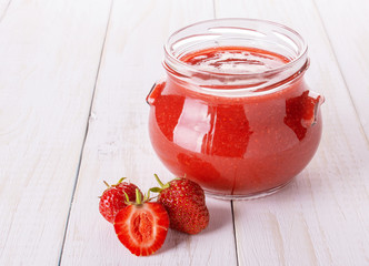 Jam from strawberries in a glass jar on white boards
