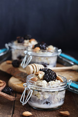Overnight oatmeal with blackberries, honey and almond milk on a rustic wood background in a canning glass bail jars with attached lid. Selective focus on oatmeal in front.