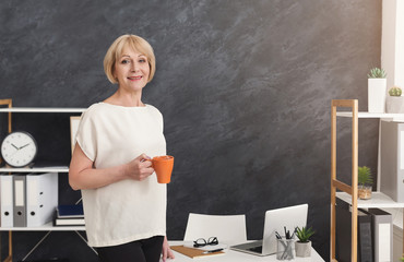 Smiling mature businesswoman with cup of coffee in the office