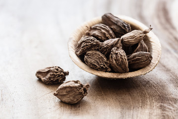 Whole black cardamom in coconut bowl on wooden background close-up