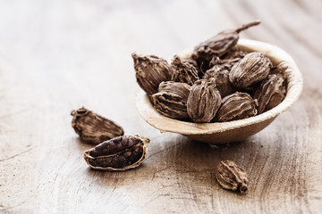 Whole black cardamom in coconut bowl on wooden background close-up