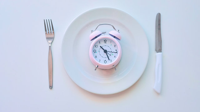 clock on an empty plate, white background. the concept of limiting the intake of food.