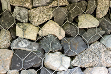 Gray stones stacked in the form of a wall and reinforced with iron grating. Light background of gravel