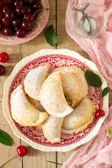 Pies with cherries, sprinkled with powdered sugar and berries of fresh cherries on a wooden surface.