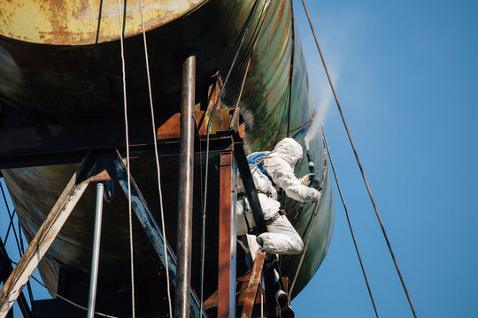 Industrial climber washing big barrel with water pressure. Risky job.