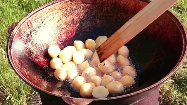 cooking small spring yellow potatoes with olive oil in a big cauldron outdoor. camping concept