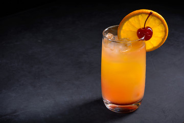 Tequila sunrise cocktail on dark stone background. With copy space.
