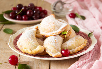 Pies with cherries, sprinkled with powdered sugar and berries of fresh cherries on a wooden surface.
