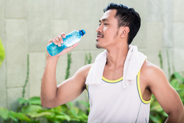 Asian man working out in his garden drinking water