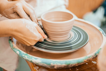 Women working on the potter's wheel. Hands sculpts a cup from clay pot. Workshop on modeling on the potter's wheel.