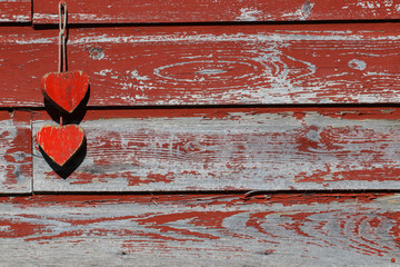 Two rustic antique red wooden hearts hanging by rope on old painted barn; blank holiday sign with copy space