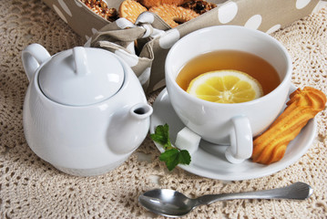 lemon tea with sweet cookies in a white cup next to the kettle