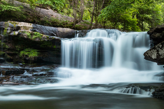 A forest waterfall with motion, large stones and green trees behind. © DSBurnside