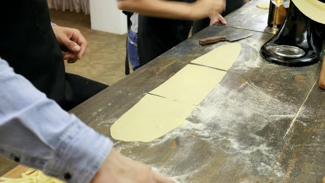 Close-up shot of female hands cutting the rolled dough on parts for pasta. 4K