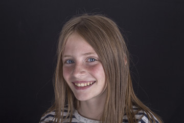 Fototapeta premium Beautiful blond young girl with freckles indoors on black background, closeup portrait