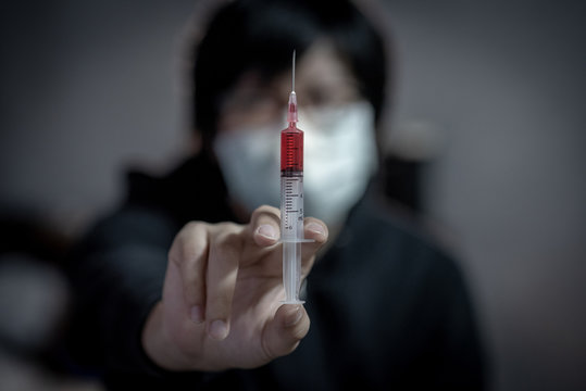 Young man in the mask using syringe for red drug injection. Drug abuse and addiction concept