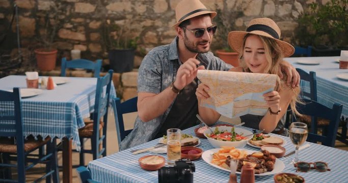 Young tourists couple reading map at traditional Greek restaurant