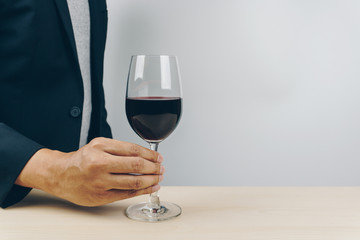 man in grey shirt and black suit putting a glass of red wine on the wooden table