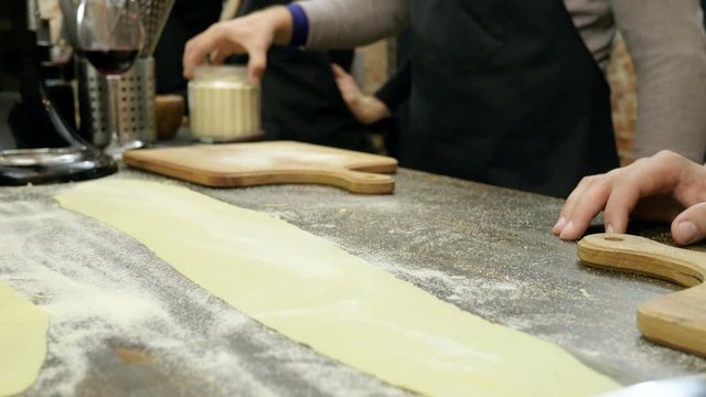 Close-up shot of male hands cutting the rolled dough on parts for the pasta. 4K